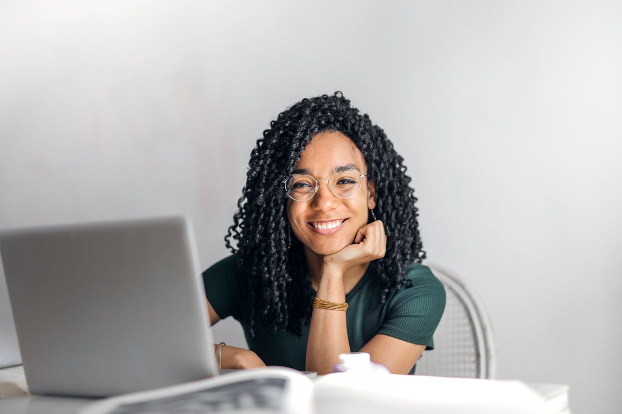 Happy ethnic woman sitting at table with laptop